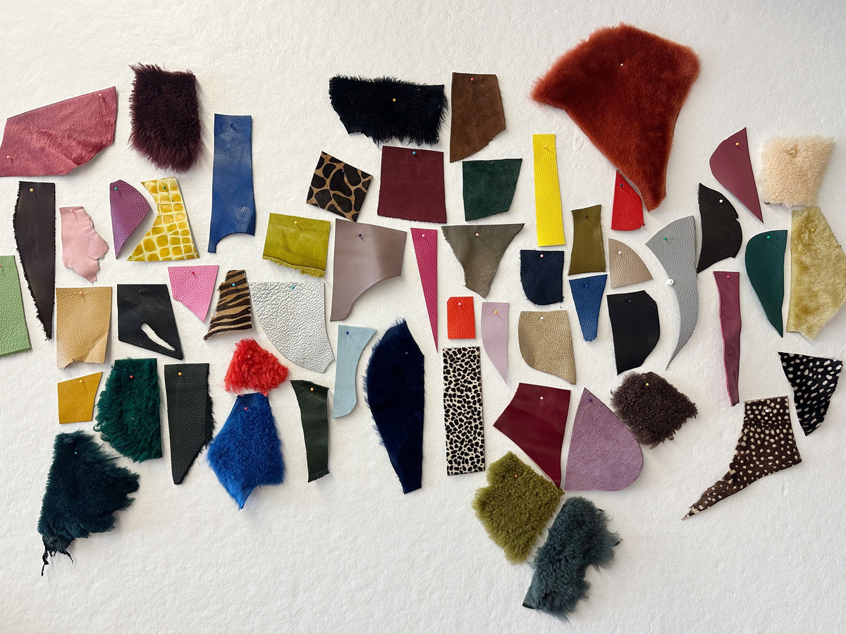 A collection of colorful leather and lambswool swatches pinned together on a white textured wall, showcasing various colors, textures, and patterns.