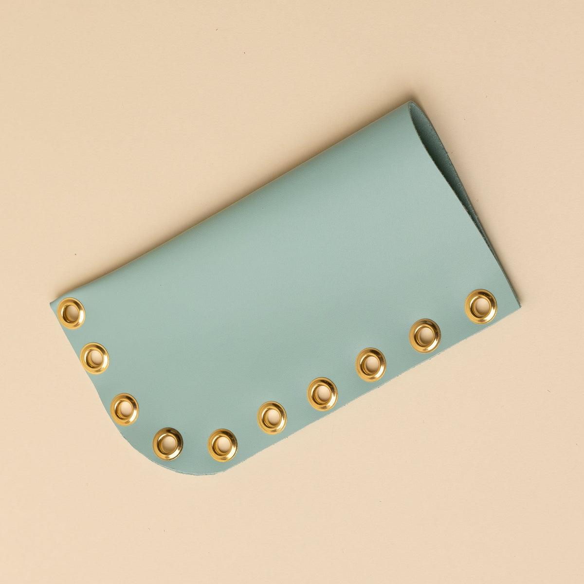 Light blue leather wallet with gold eyelets on a beige background