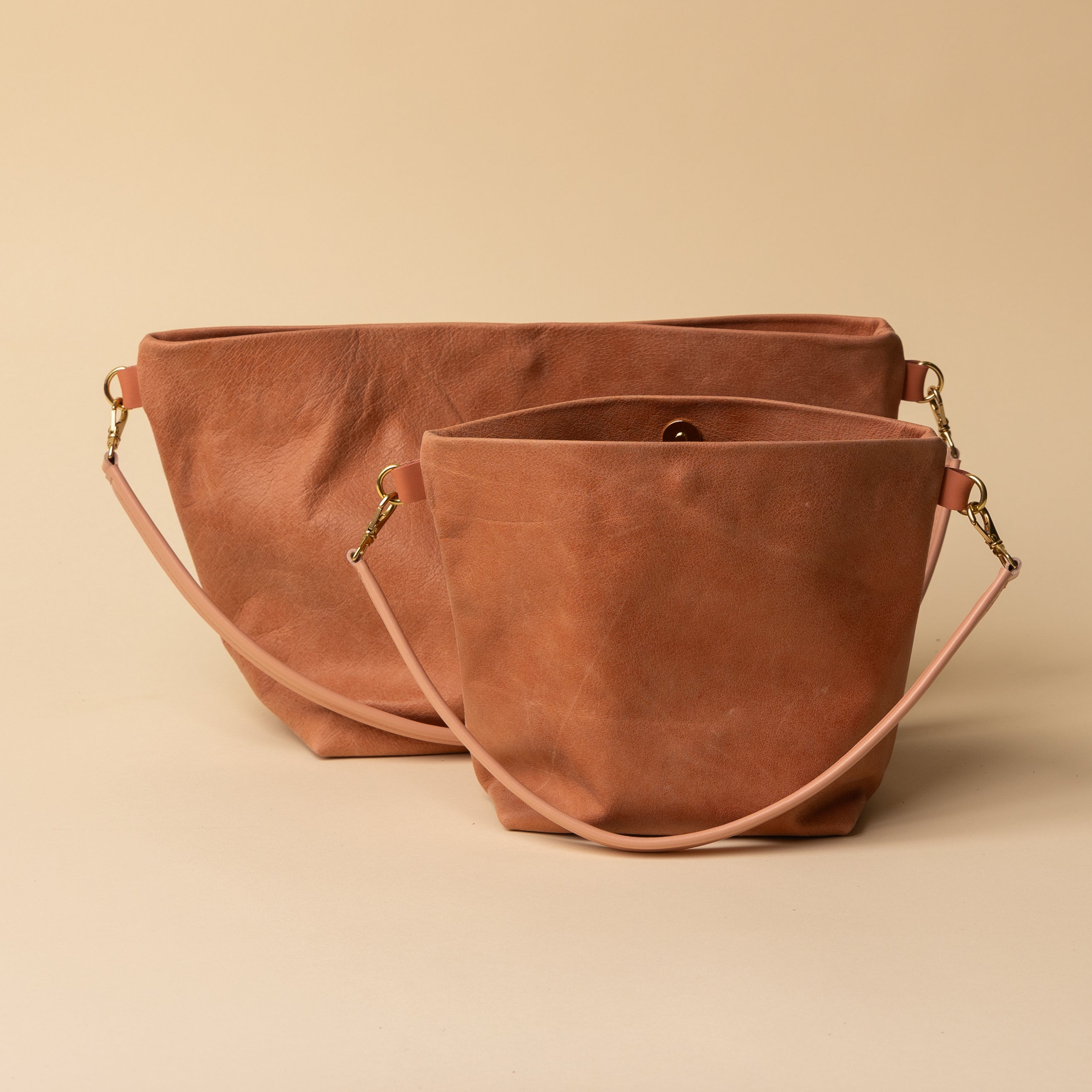 Two pale orange leather bags with gold hardware on a beige background